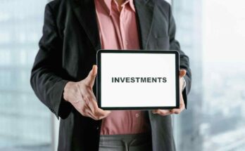 A business professional in a dark suit and red shirt hold tablet display the word ''investment'' against a blurred office style background